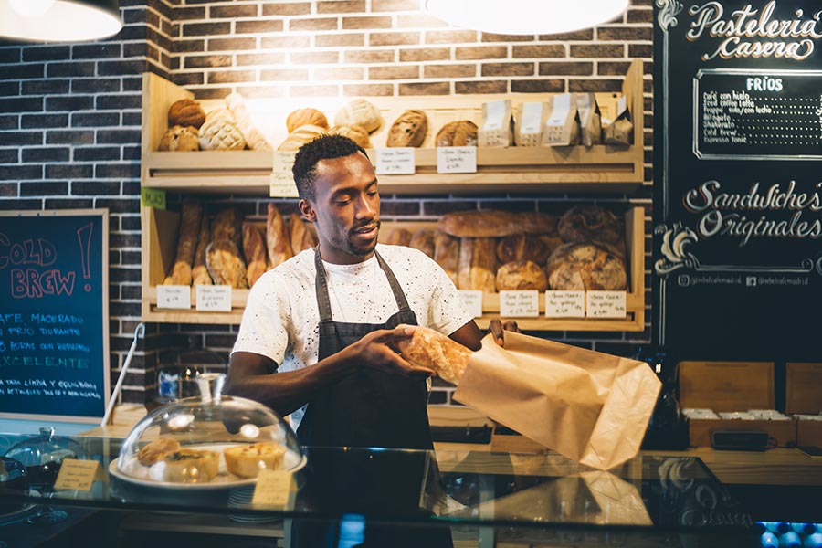 Specialized Business Insurance - Bakery Owner Bags Bread in Front of Shelves of Baked Goods